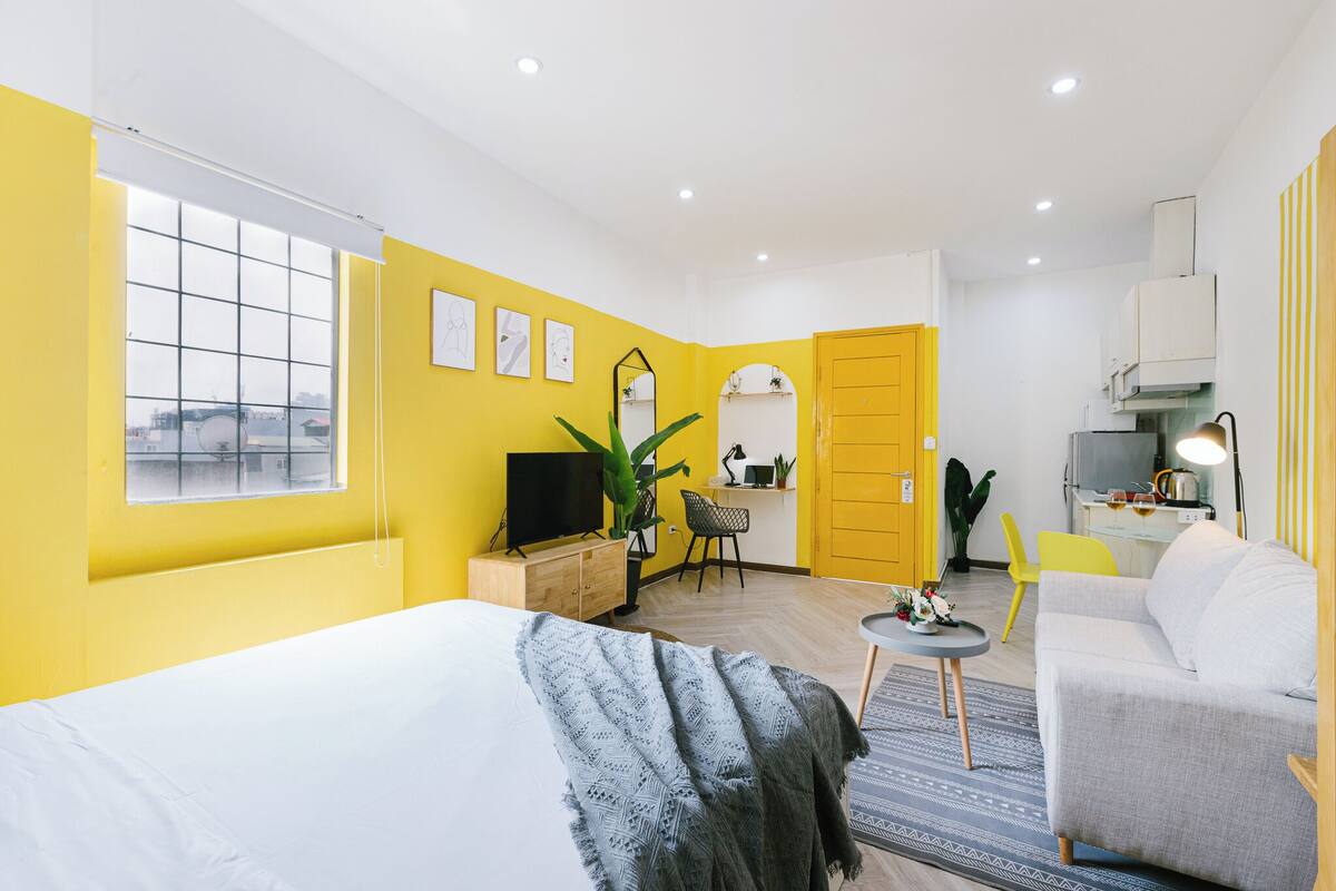 A compact hotel room with a bed, a desk, a sofa, and a small kitchen area.