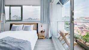 Une chambre moderne avec un grand lit, une table de chevet avec une lampe, une vue sur la ville par une grande fenêtre et un balcon agrémenté de plantes.