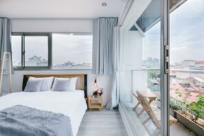 Ein modernes Schlafzimmer mit einem großen Bett, einem Nachttisch mit Lampe, Blick auf die Stadt durch ein großes Fenster und einem Balkon mit Pflanzen.