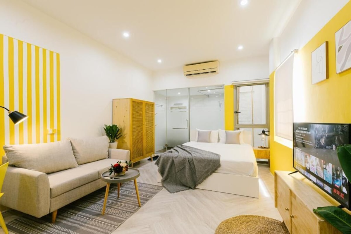A modern hotel room with a sofa, a bed, a small table, a TV, and a wardrobe.