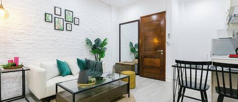 Ein modernes Wohnzimmer mit weißer Ziegelwand, einem Glastisch, einem weißen Sofa mit türkisfarbenen Kissen und einer Holztür.