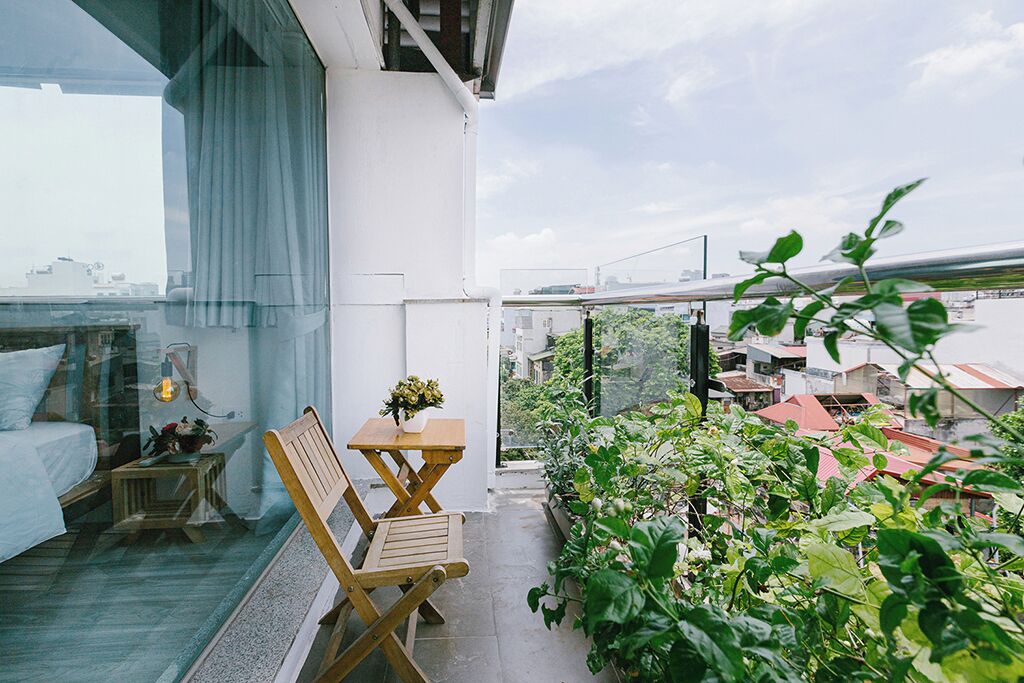 A balcony with a wooden chair, a small table with a flower vase, and potted plants.