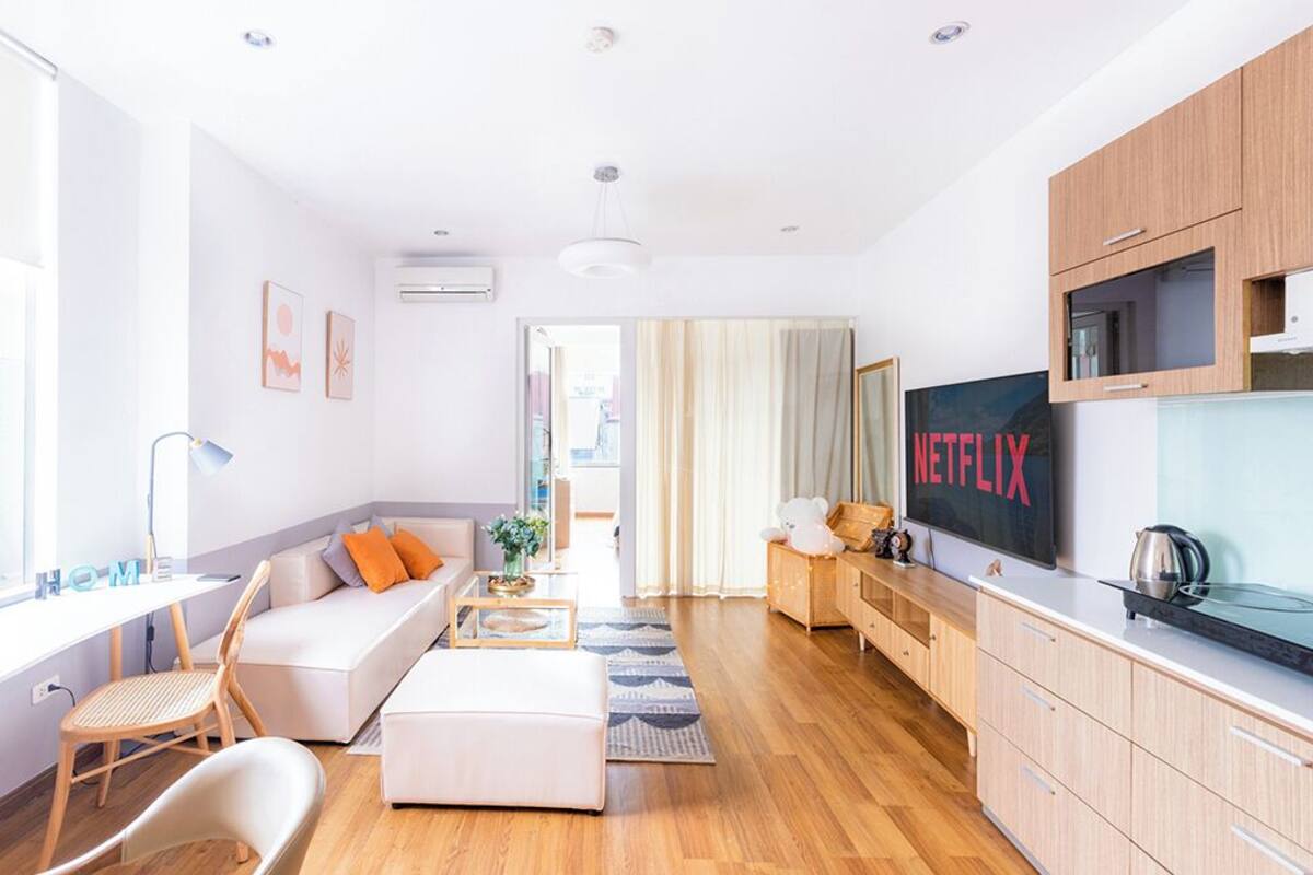 A modern living room with a sofa, ottoman, and a TV mounted on the wall.