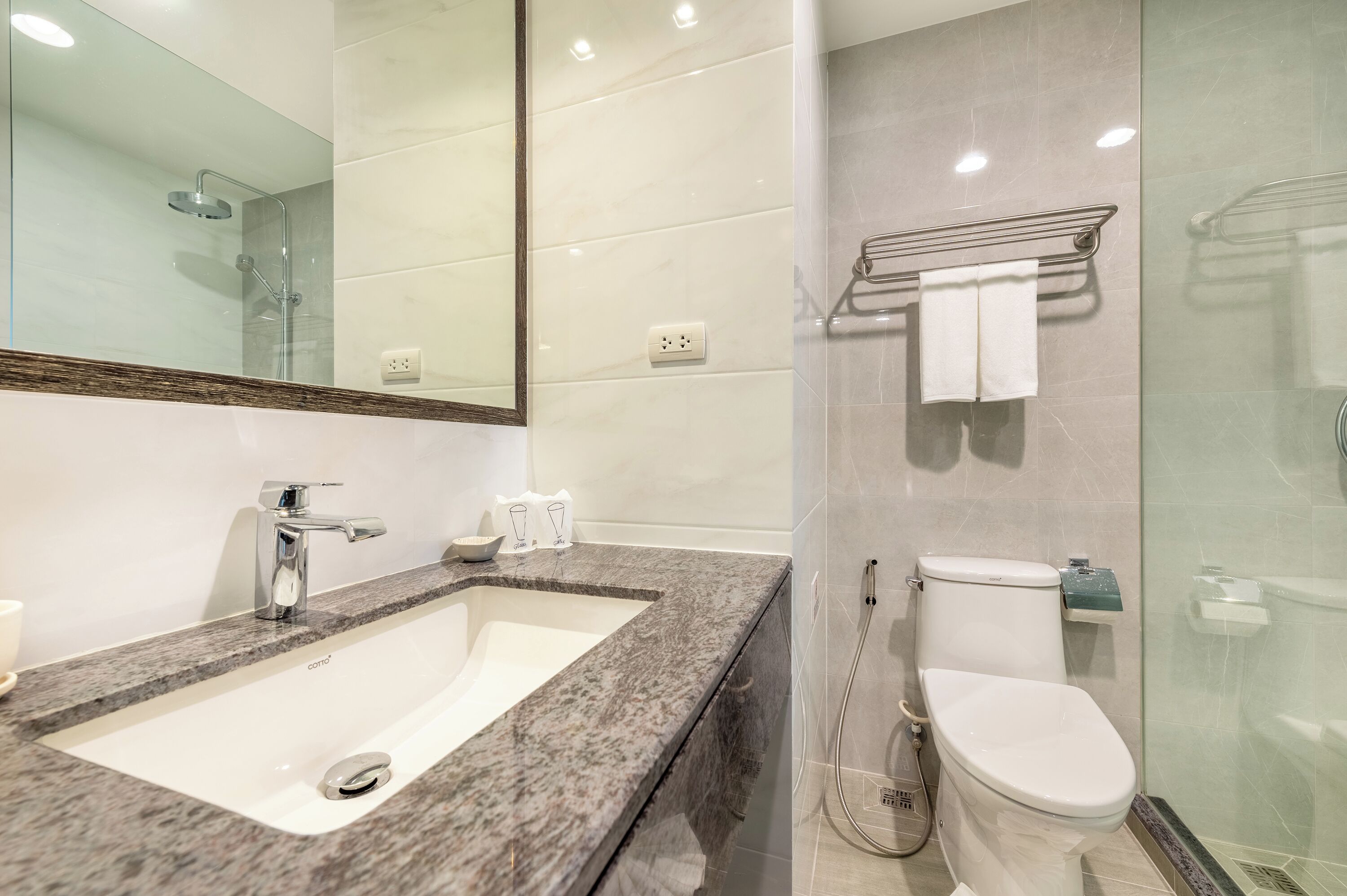 A modern bathroom with a granite countertop sink, a large mirror, a glass shower enclosure, and a toilet.