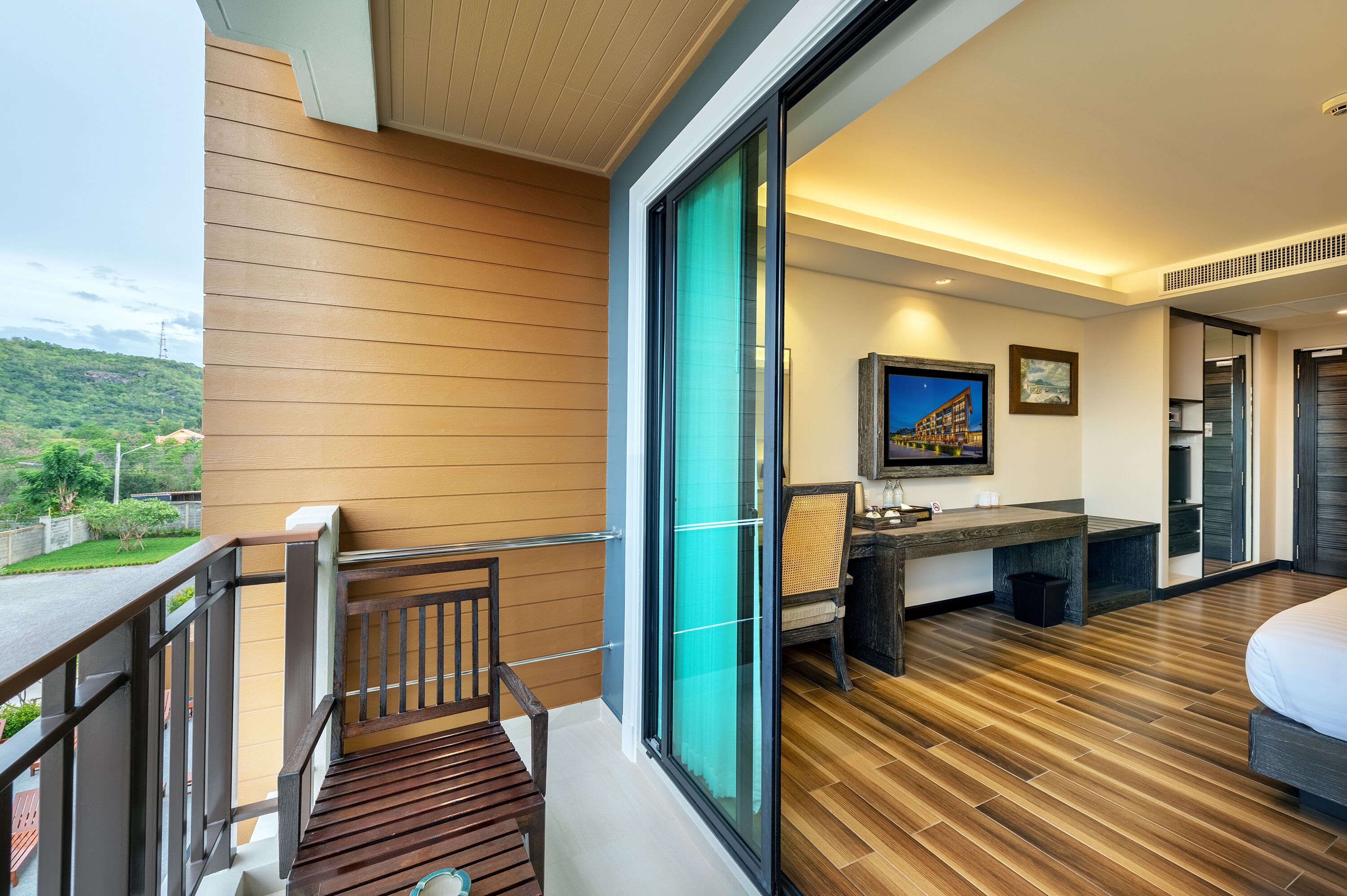 A modern hotel room with a balcony, a desk, and a bed.