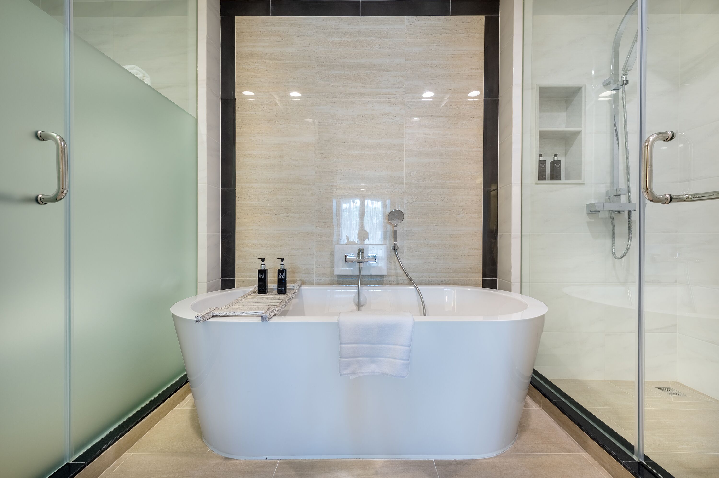 A modern bathroom with a freestanding bathtub, glass shower enclosure, and a built-in shelf with toiletries.