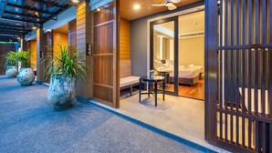 Entrada de hotel con un espacio al aire libre techado, un mostrador de recepción y una vista parcial de una habitación de huéspedes con cama y baño.