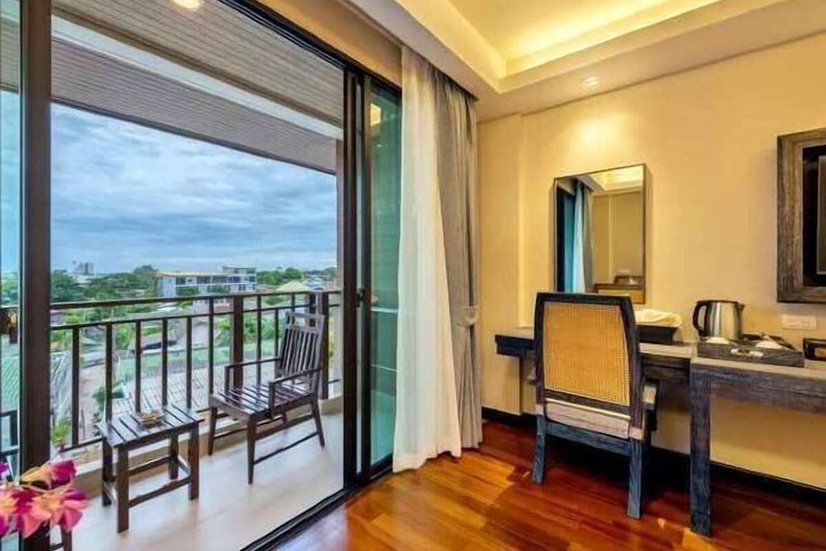 Habitación con balcón, escritorio con silla, espejo y vista al exterior.