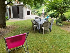 A patio with a table set for dining, surrounded by chairs, a tree, and a building in the background. - Maison de Montagne Avec Jardin Privé (Sarrancolin)