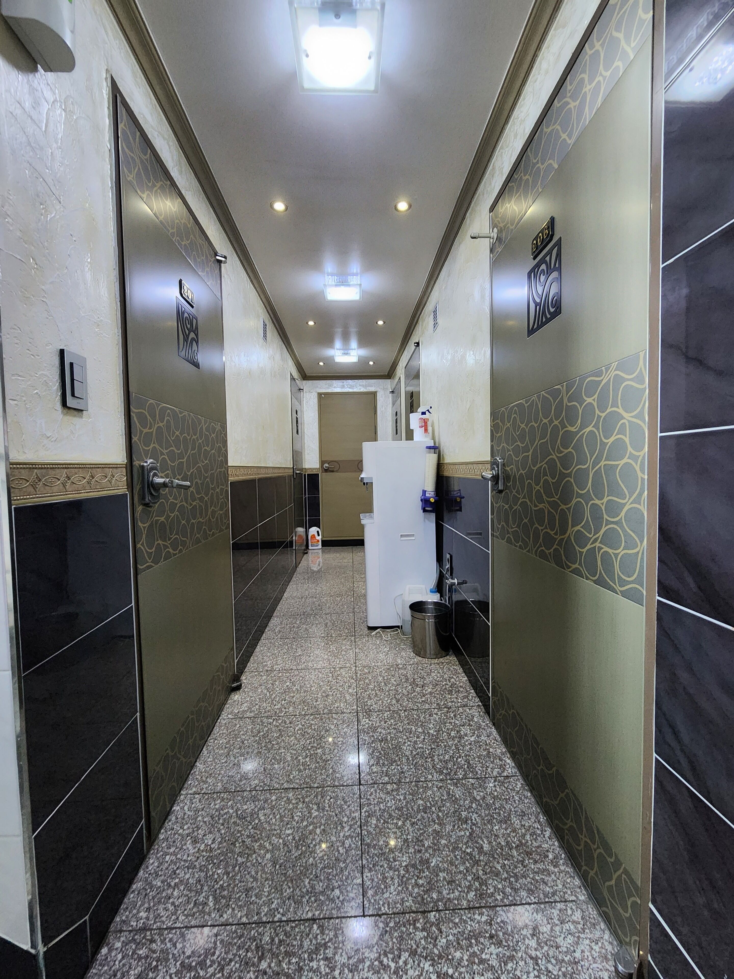 A hallway with tiled floors, doors, and a refrigerator.