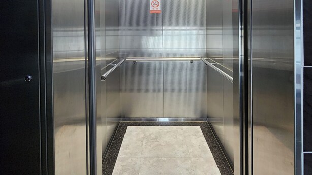 Un ascensor vacío con paredes metálicas y suelo de baldosas.