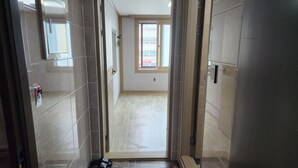 Un pasillo con paredes y suelo de baldosas, que conduce a una habitación con ventana y puerta.