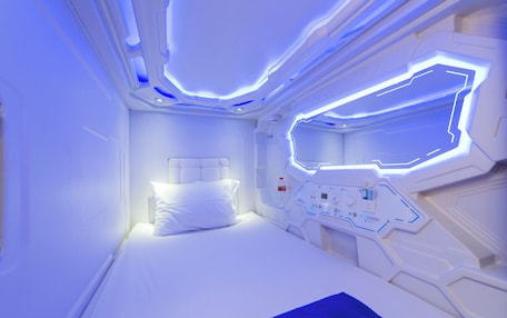 A futuristic room with a bed, control panels, and a window.