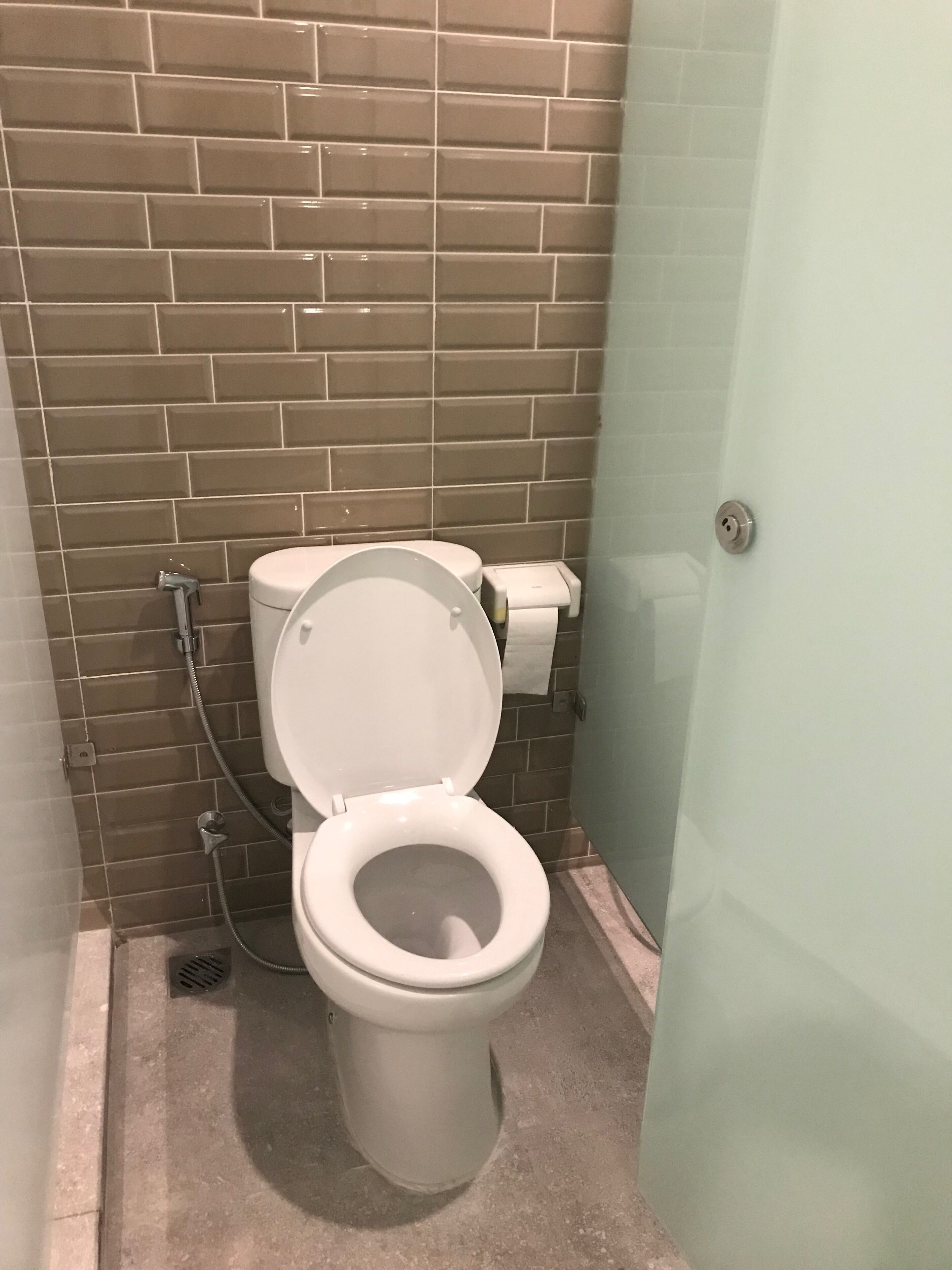 A bathroom with a toilet, a paper towel dispenser, and a shower area.