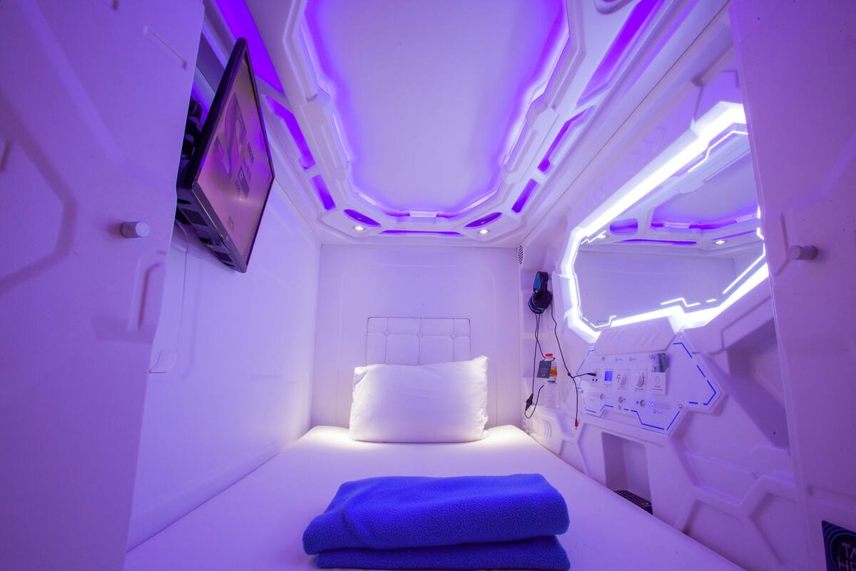 A room with a bed, a control panel, and a wall-mounted screen.