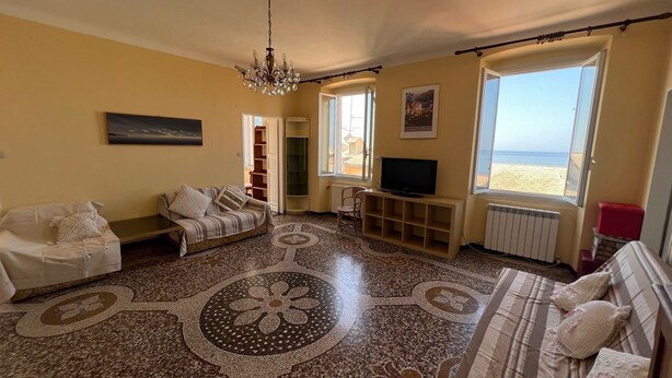 A living room with a patterned floor, a sofa, a TV stand, and a large window with a beach view. - Vast panoramic apartment 3 minutes from the sea (Camogli)