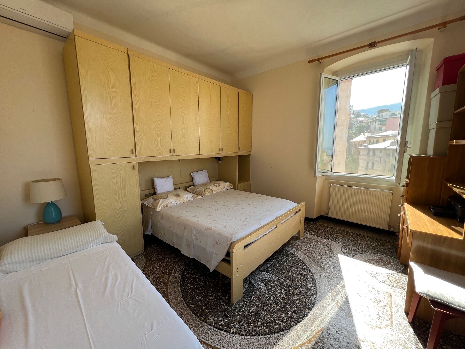 Ein Schlafzimmer mit Bett, Nachttisch, Lampe, Fenster mit Ausblick und einem eingebauten Kleiderschrank.
