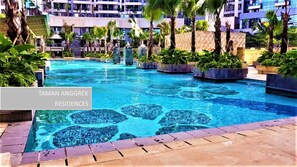 A swimming pool with a mosaic design, surrounded by palm trees and a multi-story building in the background.