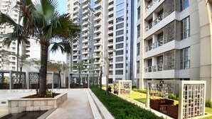 A modern residential building with multiple balconies, a central courtyard with seating, and a well-maintained garden.