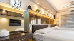 Une chambre d’hôtel moderne avec un grand lit, un bureau en bois avec un grille-pain, un téléviseur fixé au mur et un ventilateur de plafond.