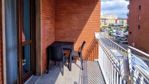 Ein Balkon mit Tisch und Stühlen, eine Schiebeglastür und Blick auf die Straße sowie umliegende Gebäude.