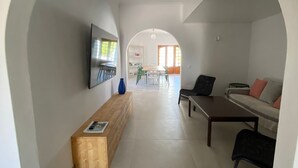 A modern interior with a wooden bench, a TV mounted on the wall, a sofa, and a dining area in the background.