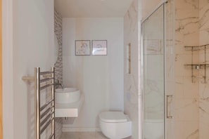 A bathroom with a glass shower enclosure, a white toilet, and a sink with a marble backsplash.