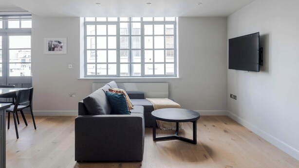 A modern living room with a sofa, a coffee table, and a TV mounted on the wall. - Clerkenwell 2-Bed · 2 Baths · Sleeps 6 (London)