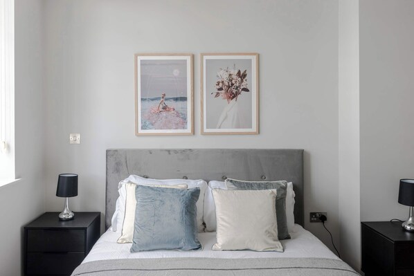 A bedroom with a bed, two bedside tables, a nightstand, and two framed pictures on the wall. - Clerkenwell 2-Bed · 2 Baths · Sleeps 6 (London)