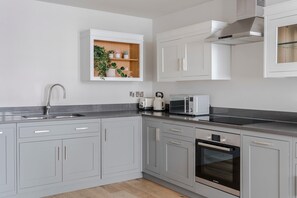 Une cuisine moderne avec des meubles gris, un four Bosch, un micro-ondes et une étagère intégrée pour les plantes.