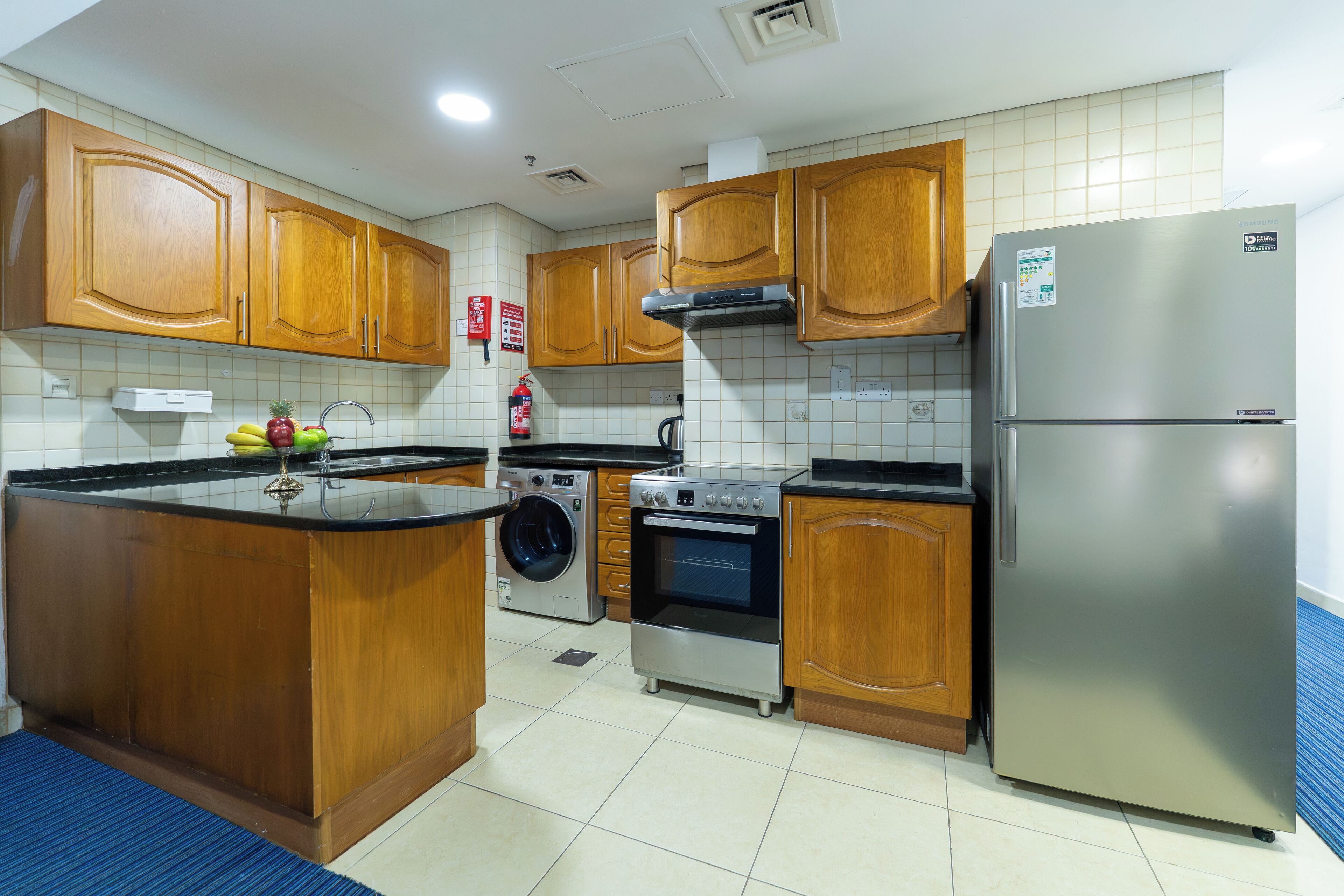 A kitchen with wooden cabinets, a stainless steel refrigerator, a washing machine, and a built-in oven.