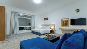 Quarto de hotel com cama, sofá, televisão e janela com cortinas.
