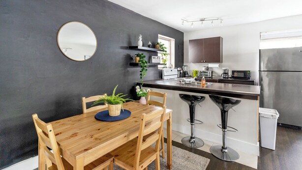 A modern kitchen with a wooden dining table, two bar stools, a refrigerator, and a microwave. - Brickell Pearl Cozy House/Beach 10 min/Location (Miami)