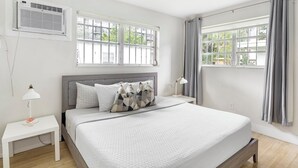 A bedroom with a bed, two bedside tables, a lamp, and an air conditioning unit. - Brickell Pearl Cozy House/Beach 10 min/Location (Miami)
