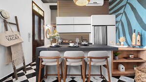 A modern kitchen with a central island, three bar stools, a hanging light fixture, and a decorative wall with a leaf pattern. - Villa Mosaico | Stylish & Modern Boutique 1 BR (San Juan)
