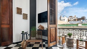A balcony with a checkered floor, a wooden door, a television, and decorative wall pieces. - Villa Mosaico | Stylish & Modern Boutique 1 BR (San Juan)