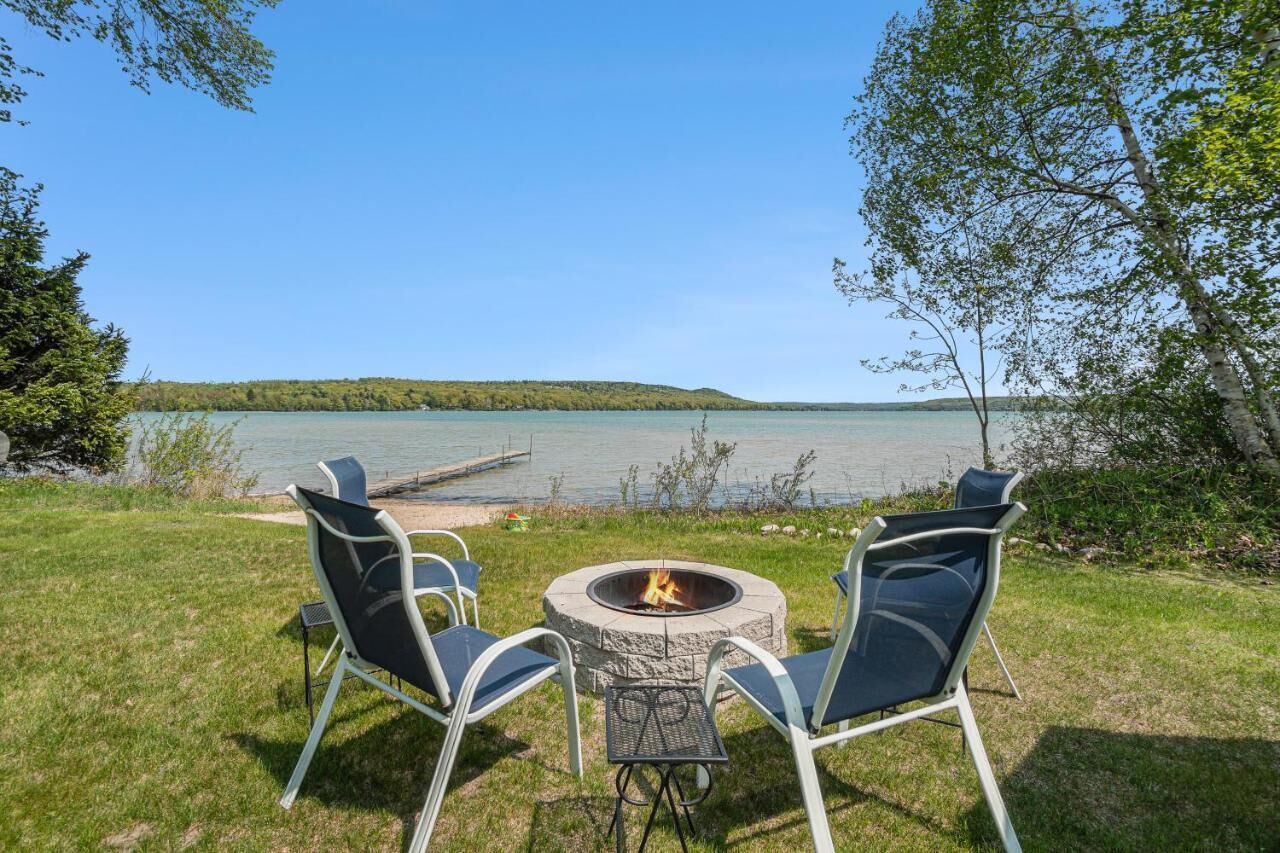 Ein Sitzbereich im Freien am Seeufer mit Feuerstelle, zwei Stühlen und einem Tisch.
