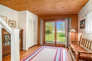 Una habitación con suelo de madera, un banco, una puerta con vistas y una estantería.