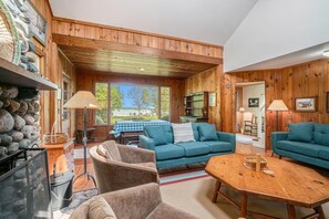 A cozy cabin interior with a blue sofa set, a wooden dining table, and a stone wall.