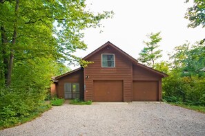 Eine eingeschossige Holzhütte mit Garage, umgeben von dichtem Grün.