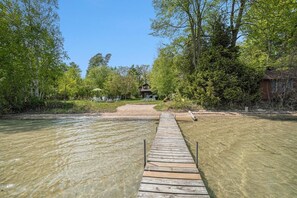 Un muelle de madera que lleva a una casa rodeada de árboles y un río.