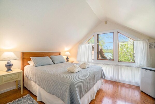 A bedroom with a large bed, a nightstand, a lamp, a window with curtains, and a radiator.