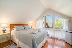 A bedroom with a large bed, a nightstand, a lamp, a window with curtains, and a radiator.