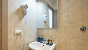 Ein Badezimmer mit Waschbecken, Föhn und Pflegeprodukten auf der Ablagefläche.