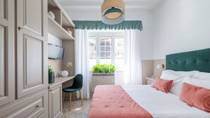 Ein Schlafzimmer mit Bett, Schreibtisch, Stuhl, Fernseher und einem Fenster mit Pflanzen.