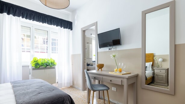 Ein Hotelzimmer mit Bett, Schreibtisch mit Stuhl, Fernseher, Spiegel und einem Fenster mit Vorhängen.