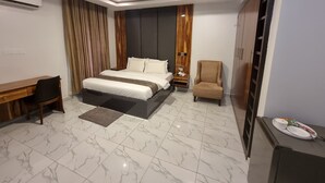 A modern hotel room with a large bed, a desk, a chair, and a wardrobe. - De James Hotels & Suites (Abuja)