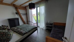 Ein Schlafzimmer mit Bett, einem kleinen Tisch mit Lampe, einem Sessel, einem Holzschrank und einem Fenster mit Vorhängen.