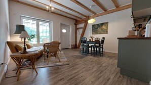 Ein großzügiger Wohnbereich mit Holzboden, einer Couch, einem Esstisch mit Stühlen und einer Küchenzeile mit einem grünen Schrank.