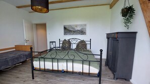 A bedroom with a bed, a dresser, a hanging plant, and a painting on the wall.